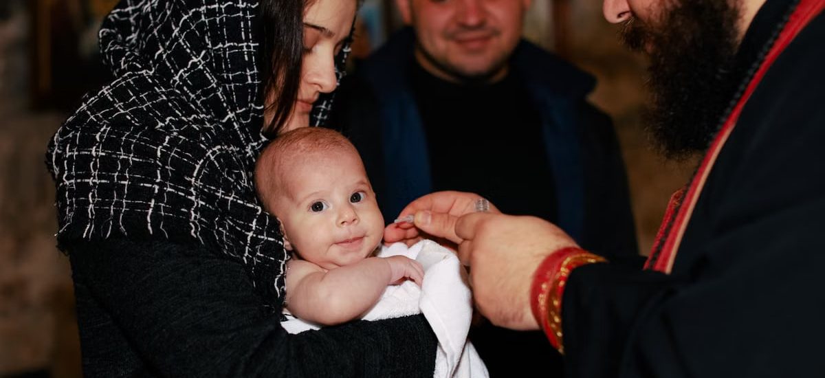 A traditional Orthodox baptism featuring a priest, baby, and family in an intimate ceremonial setting.