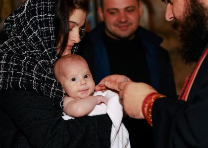 A traditional Orthodox baptism featuring a priest, baby, and family in an intimate ceremonial setting.